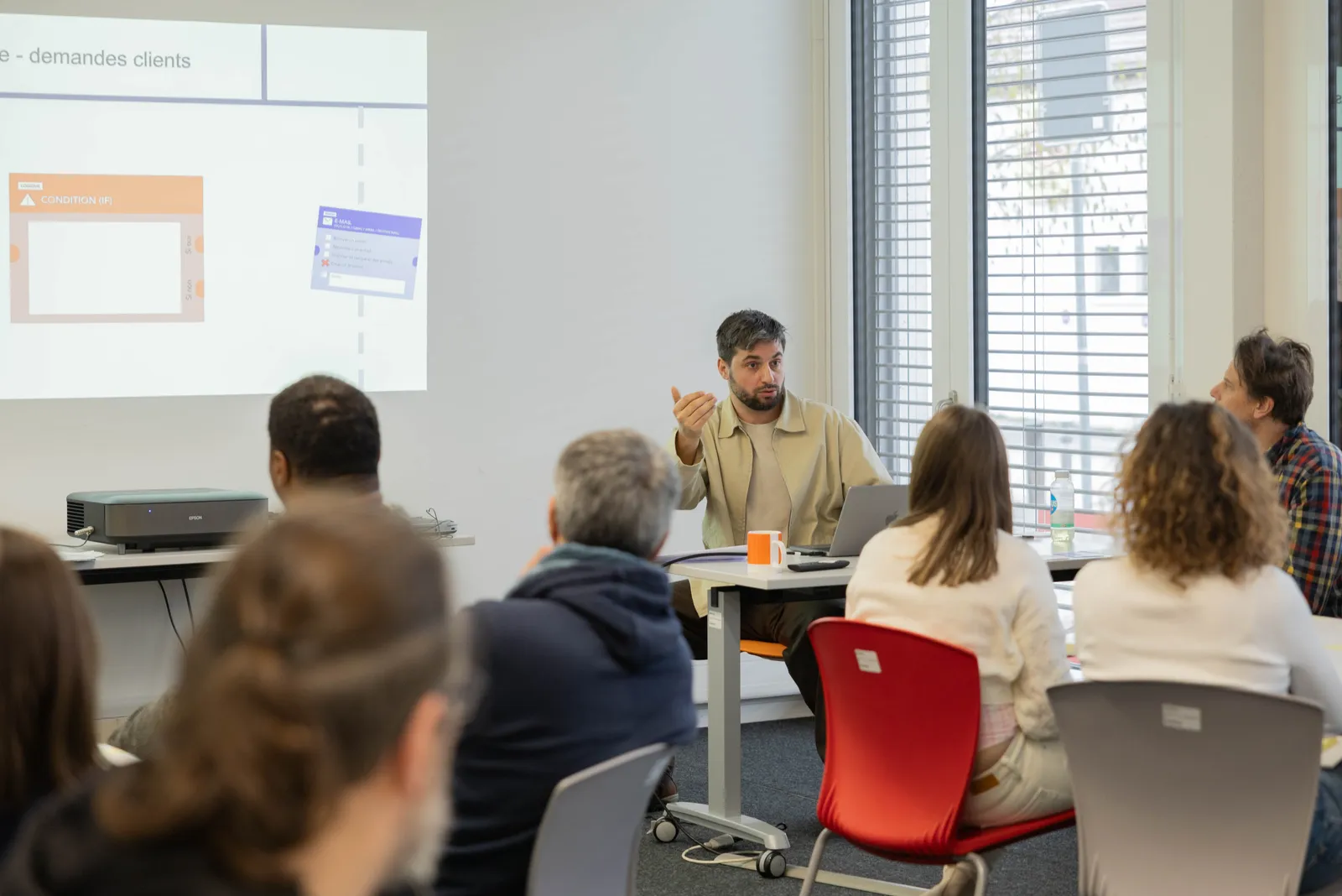 Emmanuel Bernard accompagne un petit groupe de participants devant un workflow n8n affiché à l'écran