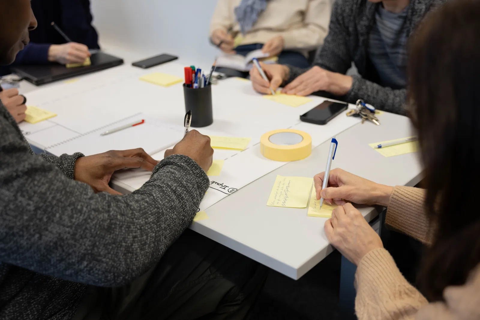 Mains de participants qui organisent des post-it sur une table pendant l'atelier du bootcamp n8n 2026